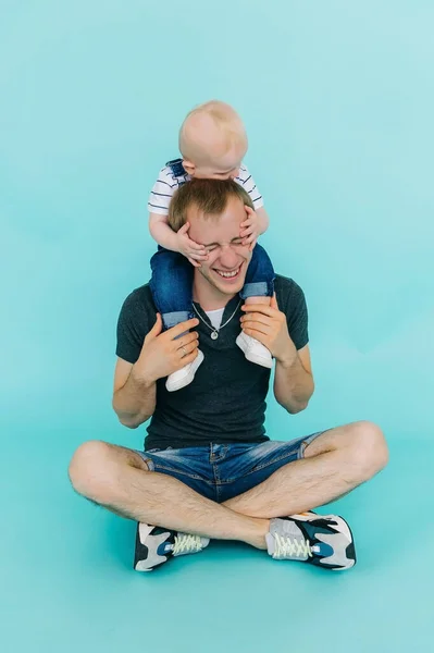 Ung pojke sitter på sin fars hals isolerad på en blå bakgrund. — Stockfoto