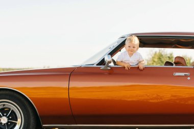 Buick Riviera tarzı. Benzersiz bir araba. Tatlı sarışın çocuk eski bir arabanın camından dışarı bakıyor.