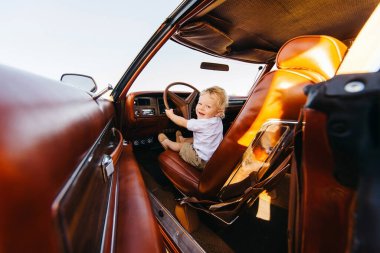Buick Riviera 'nın retro tarzı. Benzersiz bir araba. Tatlı sarışın çocuk eski bir arabanın direksiyonunda oturuyor.