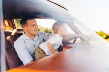 Buick Riviera 'nın retro tarzı. Benzersiz bir araba. Tatlı sarışın çocuk babasıyla birlikte eski bir arabanın direksiyonunda oturuyor.