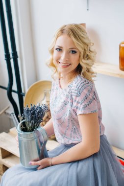 Çiçek ve metal sulama tenekesi tutan sarışın genç bir kadın balkonun içinde. Sağlıklı yaşam tarzı, güzellik, eko. Hiç atık ev kavramı.