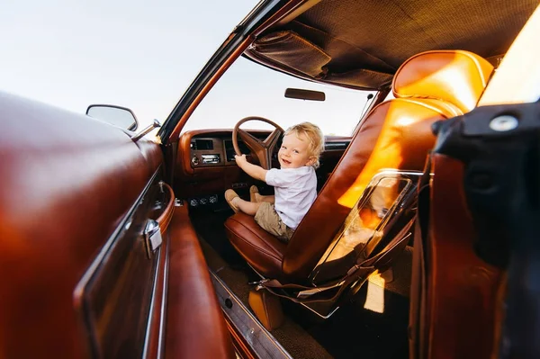 Buick Riviera 'nın retro tarzı. Benzersiz bir araba. Tatlı sarışın çocuk eski bir arabanın direksiyonunda oturuyor.