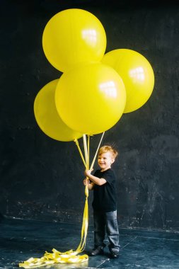 Büyük sarı balonları olan rock yıldızı çocuk. Siyah arka planda siyah elbiseli şık bir bebek