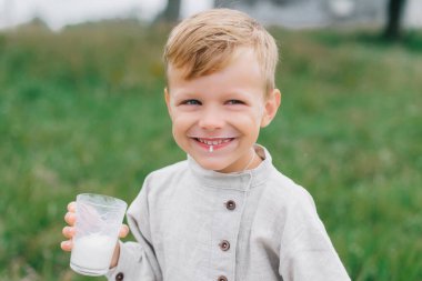 Çocuk cam bardaktan süt içiyor, süt dudaklarından akıyor. Doğada eğleniyoruz. Eko tarzı: pamuk ve keten