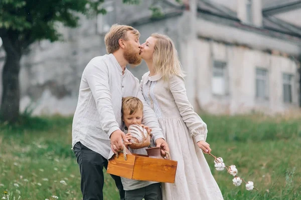 A wicker basket with bread and milk, the boy bites the bread while the parents kiss. The concept of a happy family and natural materials. Eco style: cotton and linen