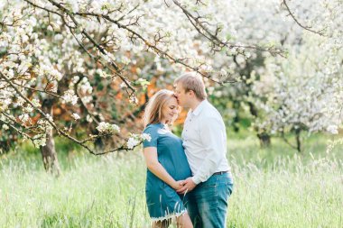 Çiçek bahçesindeki mutlu hamile bir çiftin portresi. Bir koca çiçekli bir sakura parkında karısını öpüyor. Bahar preantı