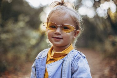 Sonbahar parkında ailesiyle yürürken fotoğraf için poz veren küçük güzel bir kız. Sonsuz mutlu ve neşeli bir çocuk, seçici odaklanma, gürültü etkisi.