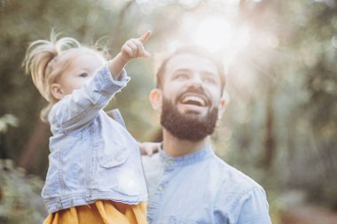 Mutlu baba-kız güzel bir sonbahar parkında yürürken oynuyorlar. Küçük kızıyla mükemmel bir hafta sonu babası. seçici odak, gürültü etkisi