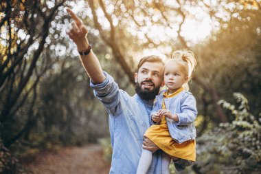 Mutlu baba-kız güzel bir sonbahar parkında yürürken oynuyorlar. Küçük kızıyla mükemmel bir hafta sonu babası. seçici odak, gürültü etkisi