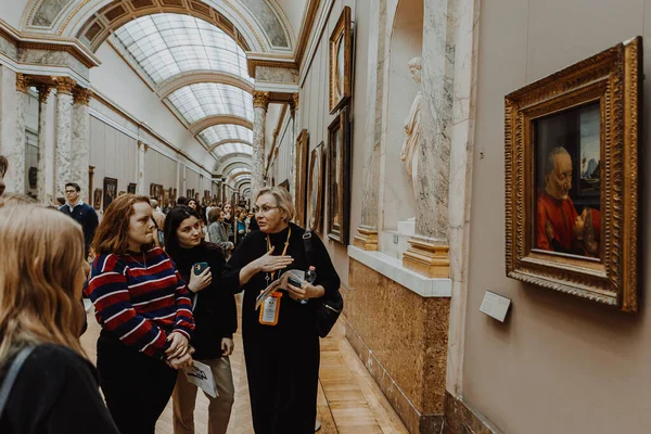 13: 02: 2020 Paris, Fransa: tur rehberi kadın Louvre 'un koridorlarında küçük bir grup genci geziyor, hikayeler anlatıyor ve resimler gösteriyor.