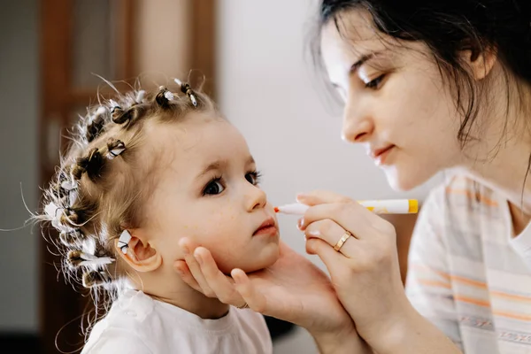 01.06.2019 Vinnitsa, Ukraine: Makeup for baby. Mom and daughter play in a beauty salon at home where mom as a makeup artist applies makeup to her happy daughter