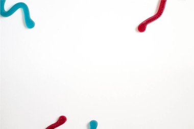 Beyaz kağıda dökülmüş solucanlar şeklinde farklı renkte jöle meyveli şekerler. Kağıt üzerinde emekleyen şekerin taklidi