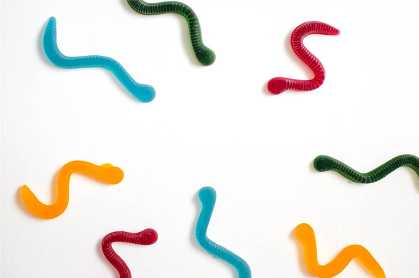 jelly fruit candies of different colors in the form of worms on a white paper background. Imitation of crawling candy on paper