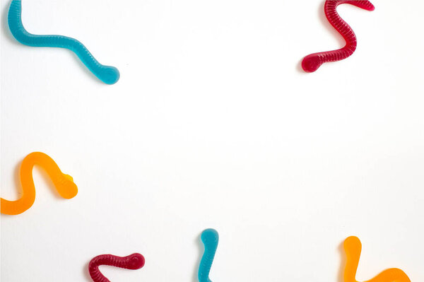 jelly fruit candies of different colors in the form of worms on a white paper background. Imitation of crawling candy on paper