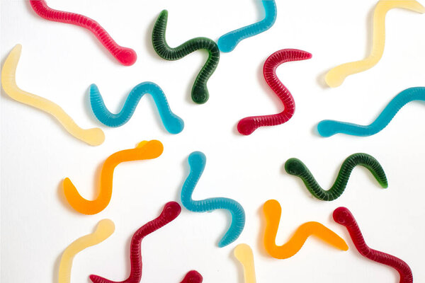 jelly fruit candies of different colors in the form of worms on a white paper background. Imitation of crawling candy on paper