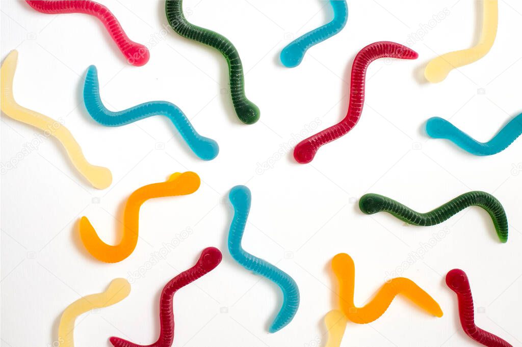 jelly fruit candies of different colors in the form of worms on a white paper background. Imitation of crawling candy on paper