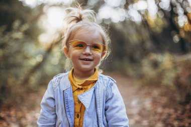 01.06.2019 Vinnitsa, Ukrayna: Sonbahar parkında ailesiyle yürürken fotoğraf için poz veren güzel bir kız, sonsuz mutlu ve neşeli bir çocuk, seçici odaklanma, gürültü efekti