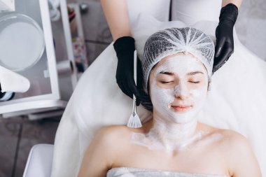 Profesyonel kozmetik uzmanının elleri kaplıca salonunda müşterinin yüzüne maske takar. Kozmetik dolabınızın veya kaplıcanızın reklamını yapmak için ideal bir ortam.