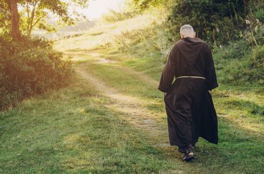 08.08.2019 Santiago de Compostela, Spain: monk of the Capuchin Order, an adult wise man with a beard and in long dark brown clothing walks the stone path in the morning in nature clipart