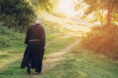 08.08.2019 Santiago de Compostela, İspanya: Capuchin Tarikatı 'nın Katolik keşişi, sakallı ve uzun koyu kahverengi elbiseli yetişkin bir adam sabah doğada taş yolda yürüyor.