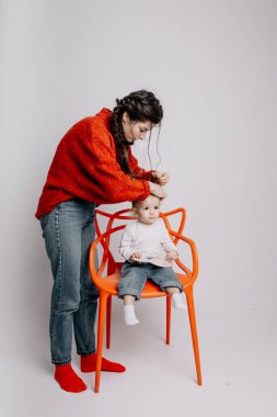 Anne ve kızı fotoğraf stüdyosunda çekimlere hazırlanıyor, anne bebeğinin saçını tarıyor.