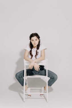 Beyaz tişört ve kot pantolon giymiş atölye ışığı önünde beyaz arka planda fotoğraf için poz veren at kuyruklu güzel bir kadın.