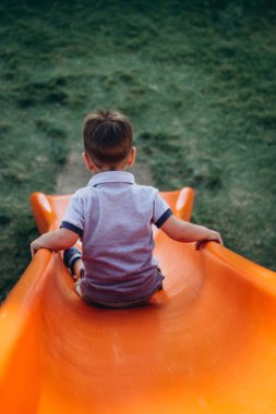 Parktaki kaydırağın üstünde küçük bir çocuk onu yakalamak isteyen bir babanın beklediği yere, aşağıya inmeye hazırlanıyor.