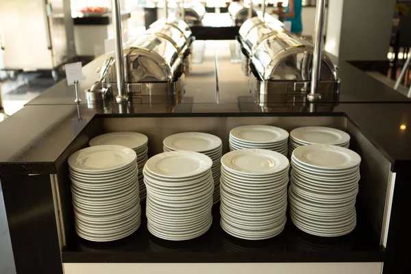 many clean plates on the counter at the buffet table in the hotel restaurant waiting for guests