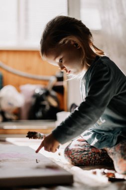 25.06.2018 Vinnitsa, Ukrane: küçük kız pencere kenarında duran kemik ve palet bıçağıyla tuvale yağlı boya çiziyor.
