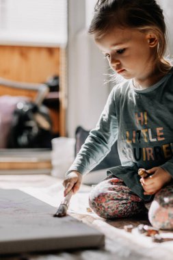 25.06.2018 Vinnitsa, Ukrane: küçük kız pencere kenarında duran kemik ve palet bıçağıyla tuvale yağlı boya çiziyor.