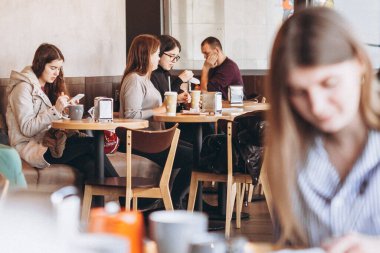 05.02.2020 Vinnitsa, Ukrayna: zarif gülüşü ve güzel gözleri olan bir kadın arkadaşıyla samimi bir kafede kahvaltı yapıyor. Masada bir sandalyede oturup latte içer.