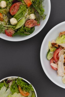 Gri arka plana sosla karıştırılmış taze salata içerikli beyaz tabaklar. Menü, pankart veya reklam için bir yer