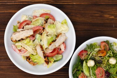 Çekici bir arkaplana yerleştirilmiş sosla karıştırılmış taze salata içerikli beyaz tabaklar. Menü, pankart veya reklam için bir yer