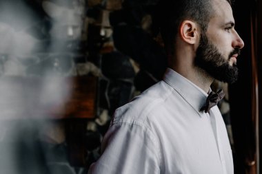 Bıyıklı ve eski püskü smokinli şık genç Gürcü adam eski evin arka planında bir fotoğraf için poz veriyor.