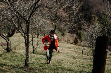 Bahar bahçesinde genç bir adam ev şöminesi için odun topluyor ve kesiyor.