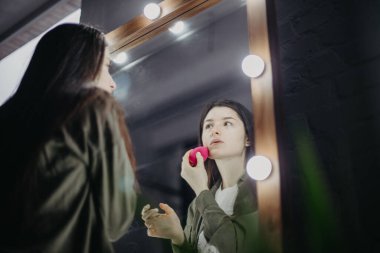 Lüks güzellik salonunda büyük aynaları ve aydınlığı olan şık bir kız makyaj yapıyor.