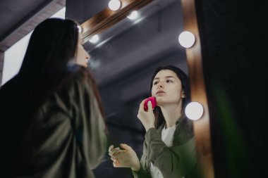 Lüks güzellik salonunda büyük aynaları ve aydınlığı olan şık bir kız makyaj yapıyor.