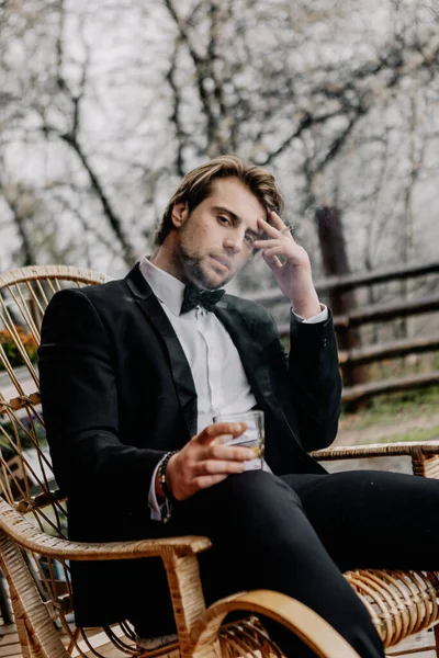 スーツに身を包んだ勇敢な残忍な男強いアルコールとタバコを手に家の裏庭に座って — ストック写真