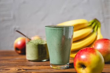 Sağlıklı bir işletme için meyve kokteylinin tanıtım çekimi. Fotoğrafta, meyve ve alg spirulinasından yapılmış yeşil bir içecek bardağı var.