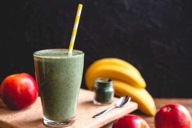 Sağlıklı bir işletme için meyve kokteylinin tanıtım çekimi. Fotoğrafta, meyve ve alg spirulinasından yapılmış yeşil bir içecek bardağı var.