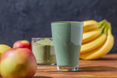 Sağlıklı bir işletme için meyve kokteylinin tanıtım çekimi. Fotoğrafta, meyve ve alg spirulinasından yapılmış yeşil bir içecek bardağı var.