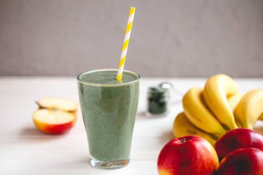 Sağlıklı bir işletme için meyve kokteylinin tanıtım çekimi. Fotoğrafta, meyve ve alg spirulinasından yapılmış yeşil bir içecek bardağı var.