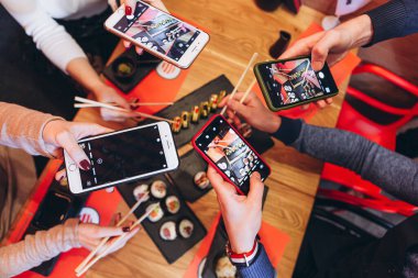 23.03.2020 Kyiv, Ukrayna: birçok akıllı telefon, masada bir dizi rol oynayan bir arkadaş şirketinin elinde. Mutlu arkadaşlar Japon restoranında suşi yiyorlar. 
