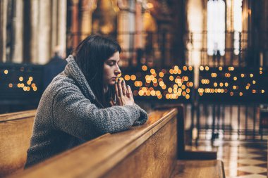 Kadim bir Katolik tapınağında diz çöküp dua eden bir kadın. Boşluğu kopyala