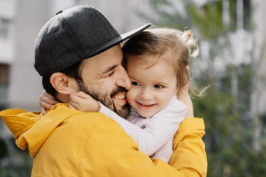 Güzel bir babanın ve küçük kızının portresi. Çok katlı bir binanın bahçesinde yürüyüşe çıkmışlar.