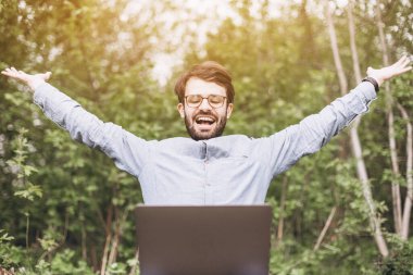 Doğada dizüstü bilgisayarı olan şık bir genç adam. Mesafeli çalışma ve seyahat, yaşam tarzı konsepti olarak serbest çalışma.