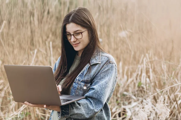 Young woman working with laptop on nature.  Outdoors nature journey and relaxation. Freelance work concept.