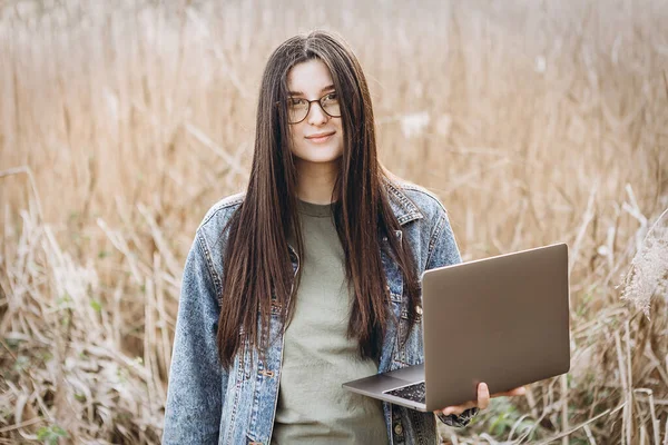 Young woman working with laptop on nature.  Outdoors nature journey and relaxation. Freelance work concept.