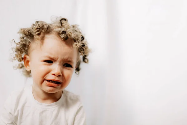 Little curly girl is crying very emotionally, face with tears and negative emotions of disappointment and insult. Baby emotions and baby crying