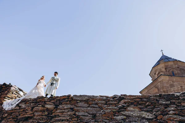 조지아 신랑은 결혼식이 교회와 하늘을 배경으로 절벽에서 신부를 이끌고 — 스톡 사진